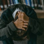 Person sitting with head down and hands on head in a library setting.